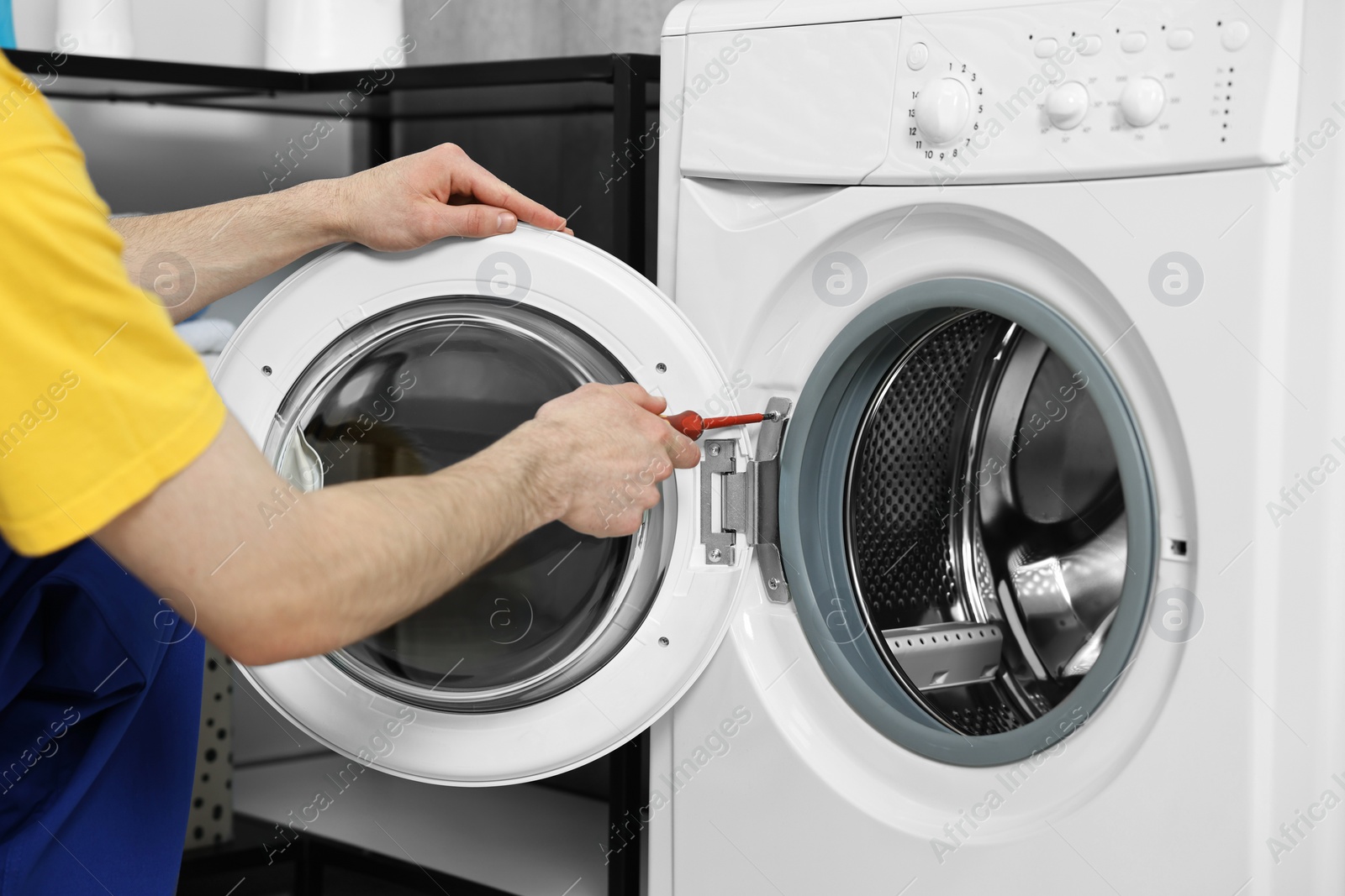 Photo of Plumber repairing washing machine with screwdriver indoors, closeup