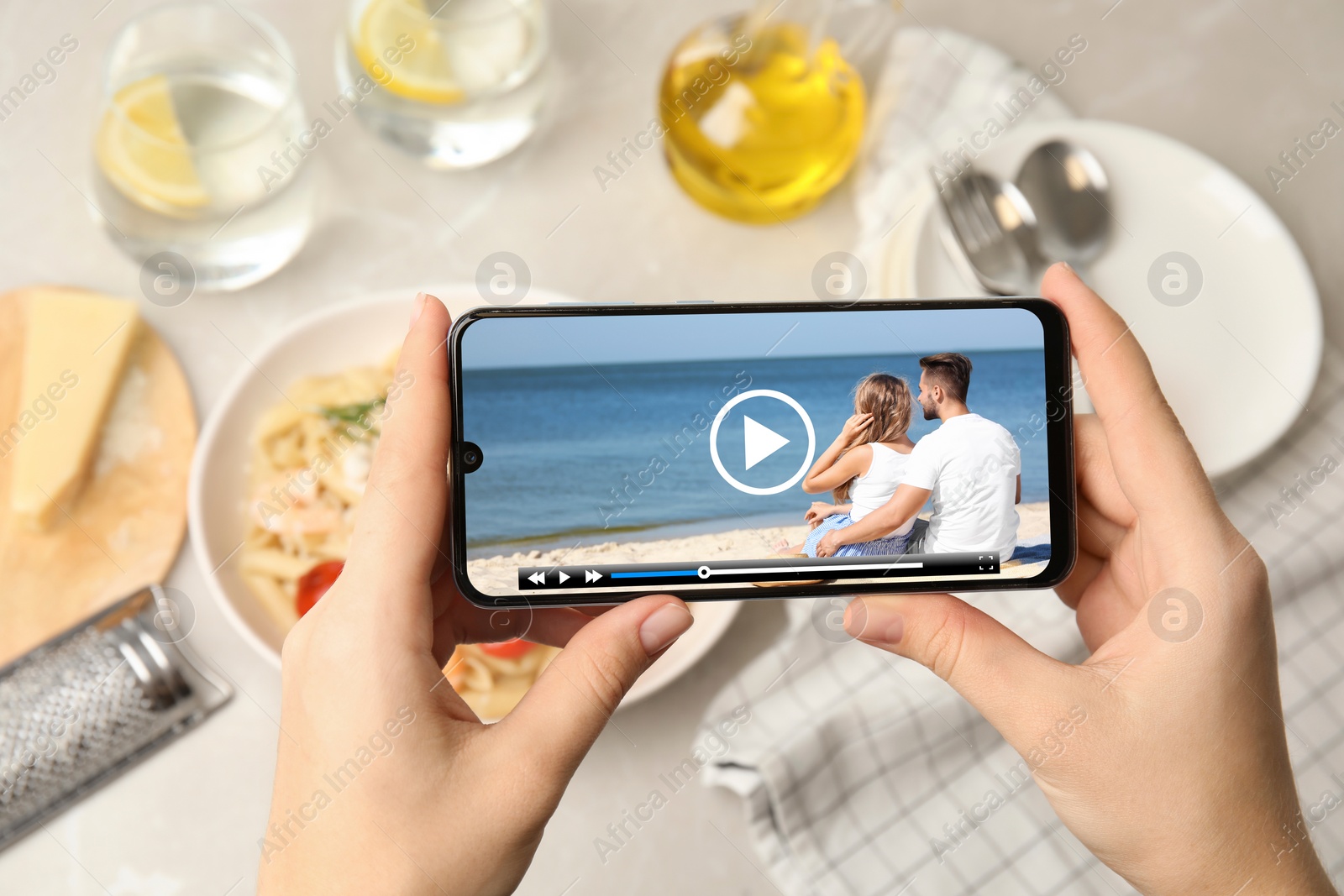 Image of Woman watching video on mobile phone at table during lunch, closeup