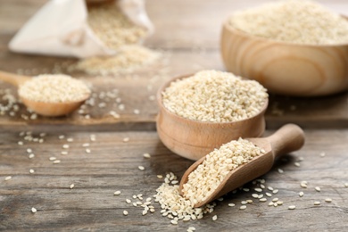 Bowl and scoop with sesame seeds on wooden table. Space for text