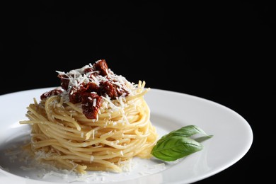 Photo of Tasty spaghetti with sun-dried tomatoes and parmesan cheese on plate against black background, closeup. Exquisite presentation of pasta dish