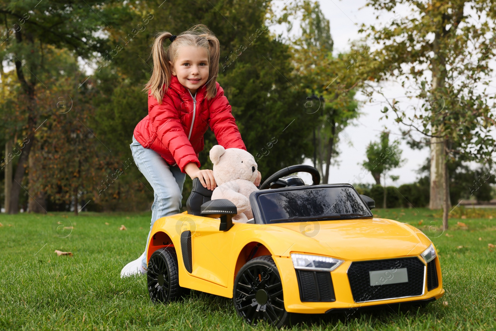 Photo of Cute little girl playing with toy bear and children's car in park