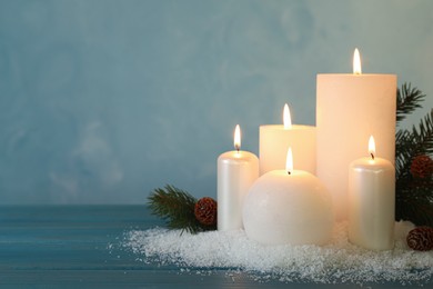 Photo of Burning candles with fir tree branch, cones and artificial snow on blue wooden table, space for text. Christmas atmosphere