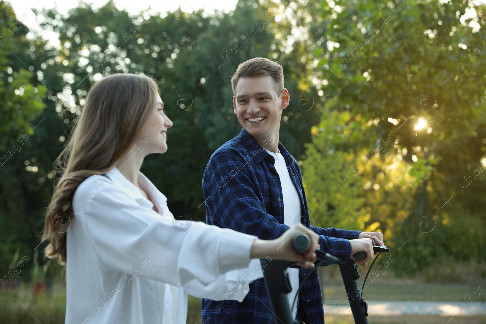 Photo of Happy couple riding modern electric kick scooters in park