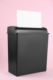 Shredder with sheet of paper on pink background