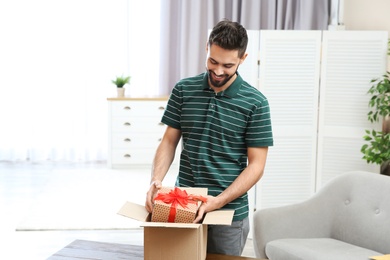 Young man opening parcel on table at home