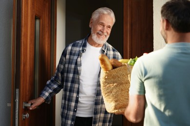 Man with wicker bag of products helping his senior neighbour outdoors