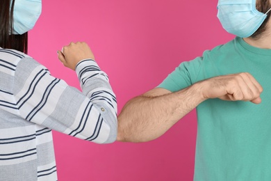 Photo of Man and woman bumping elbows to say hello on pink background, closeup. Keeping social distance during coronavirus pandemic