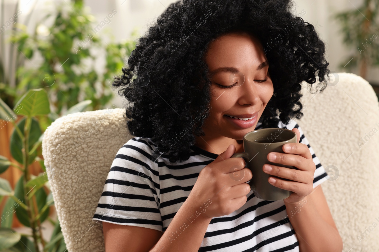 Photo of Relaxing atmosphere. Woman with cup of hot drink near houseplants at home