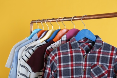 Photo of Rack with stylish children clothes on yellow background, closeup