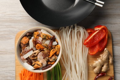 Photo of Black wok and board with products on light wooden table, top view