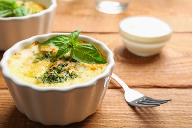 Photo of Tasty broccoli casserole in ramekin on wooden table, closeup