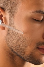 Photo of Handsome man applying cosmetic serum onto face, closeup