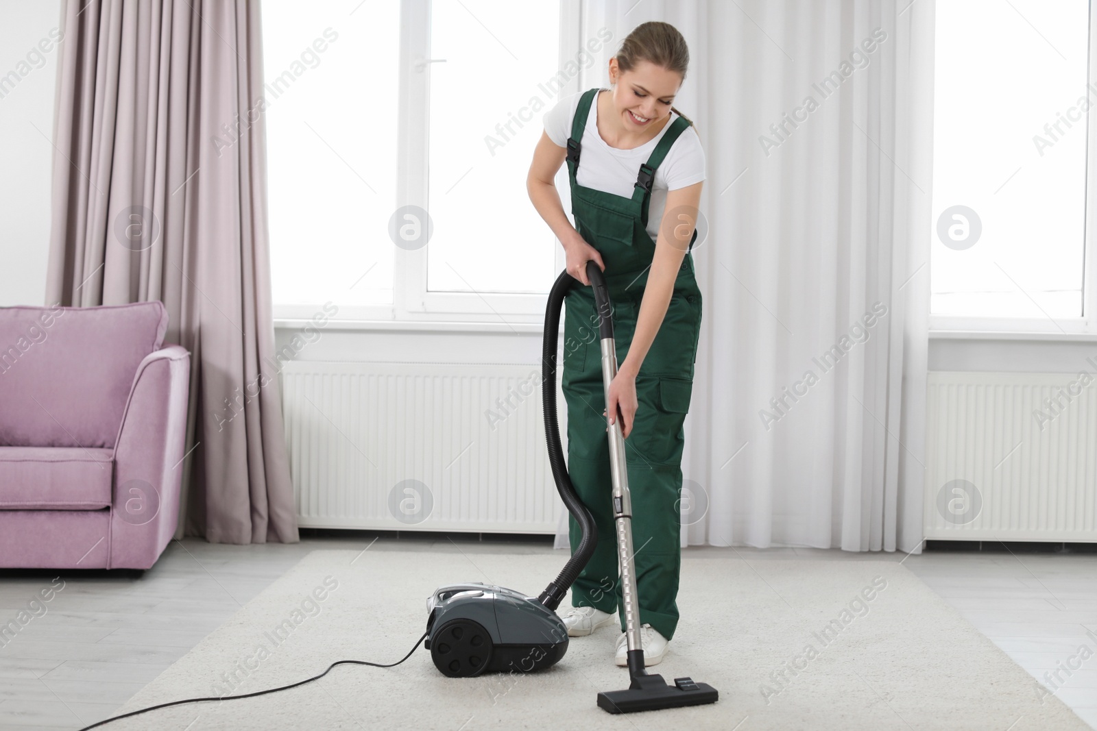 Photo of Female worker cleaning carpet with vacuum in living room
