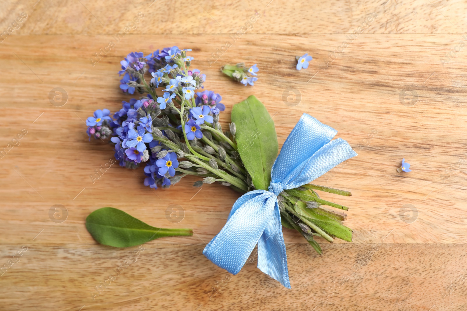 Photo of Beautiful blue forget-me-not flowers tied with ribbon on wooden table, flat lay