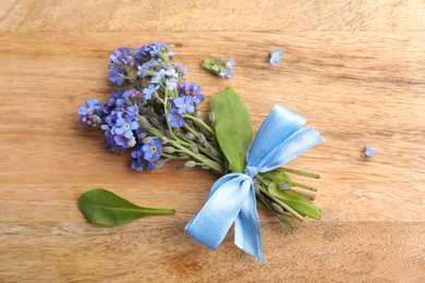 Beautiful blue forget-me-not flowers tied with ribbon on wooden table, flat lay