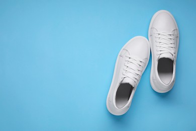 Photo of Pair of stylish white sneakers on light blue background, top view. Space for text