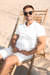 Photo of Young man relaxing in deck chair on sandy beach