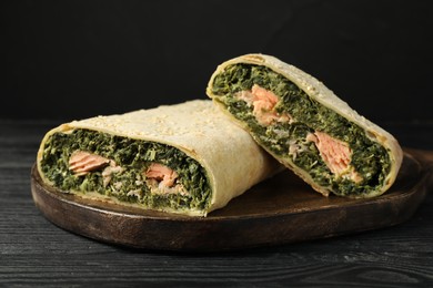 Photo of Tasty strudel with salmon and spinach on black wooden table, closeup