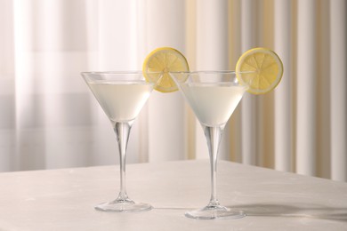 Martini glasses with fresh cocktail and lemon slices on beige marble table indoors