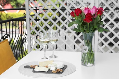 Beautiful roses, glasses of wine and snacks on white table at balcony