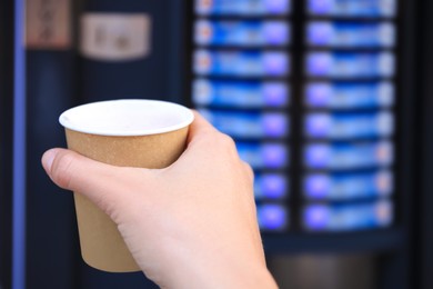 Photo of Man holding paper cup with hot drink near coffee vending machine, closeup. Space for text
