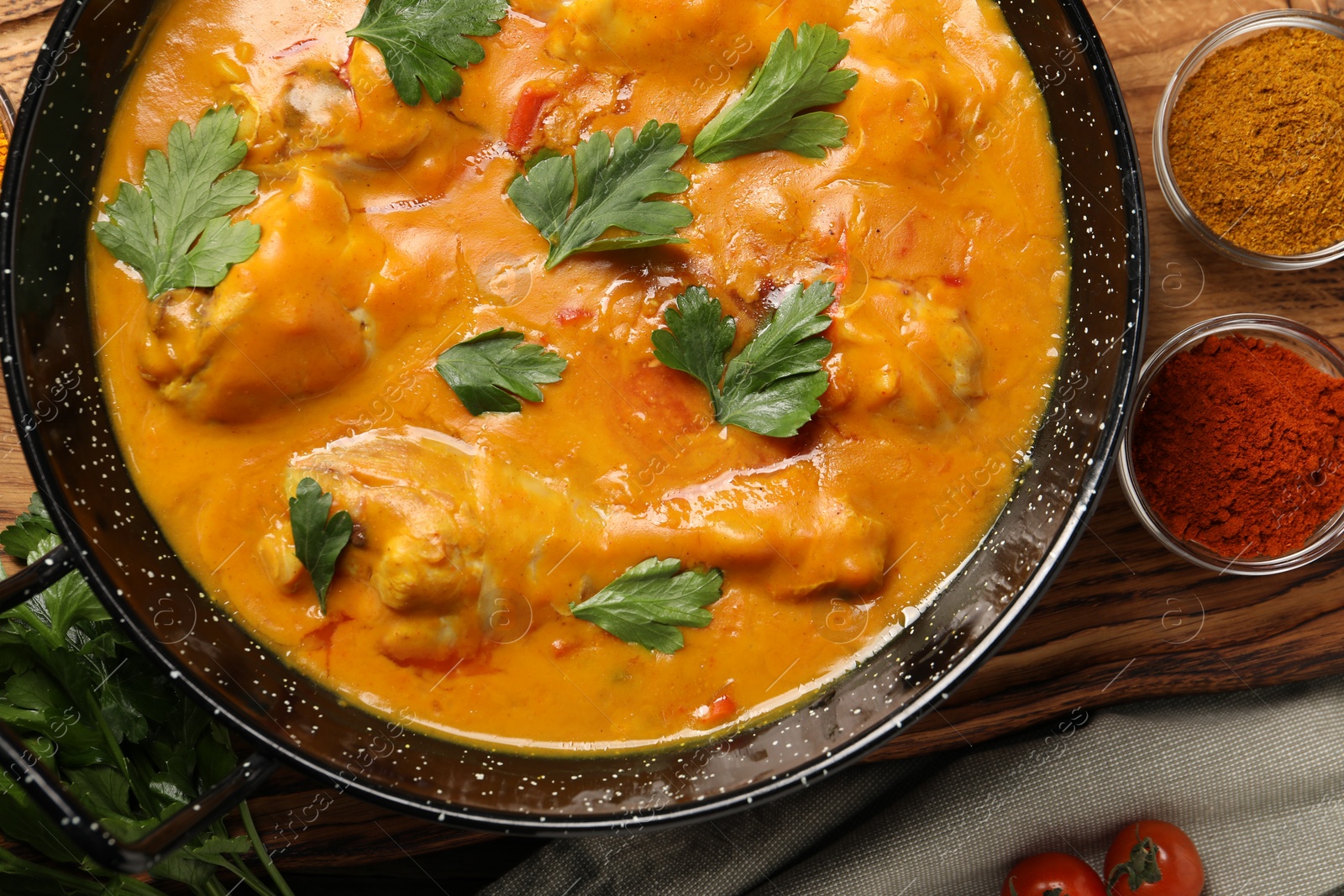 Photo of Tasty chicken curry with parsley and ingredients on wooden table, flat lay