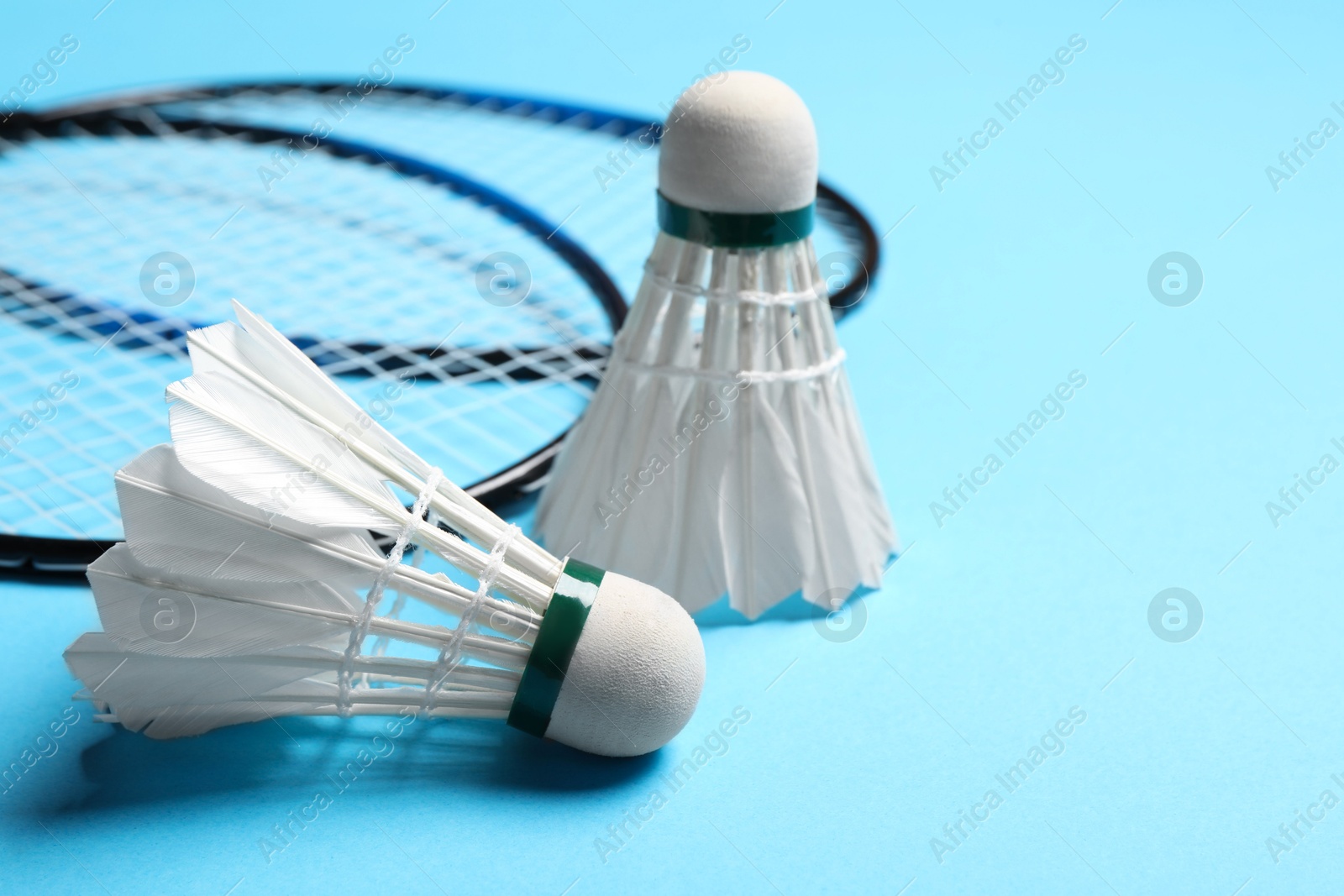 Photo of Feather badminton shuttlecocks and rackets on light blue background, closeup. Space for text