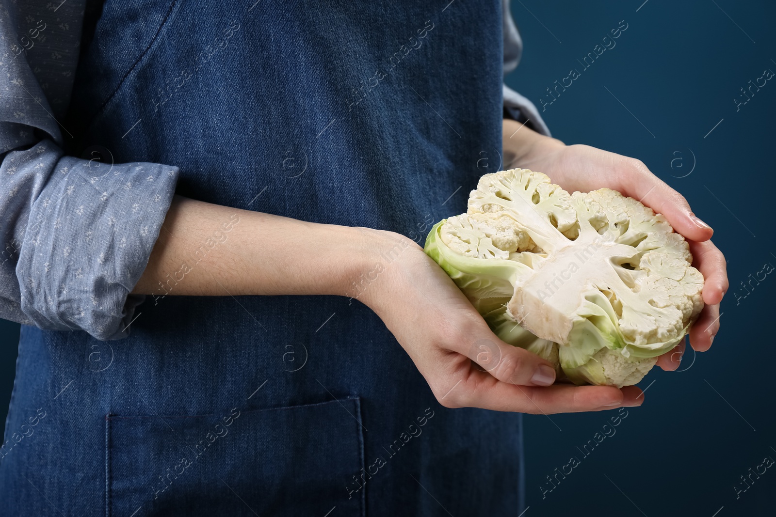 Photo of Woman holding fresh cauliflower against dark blue background, closeup