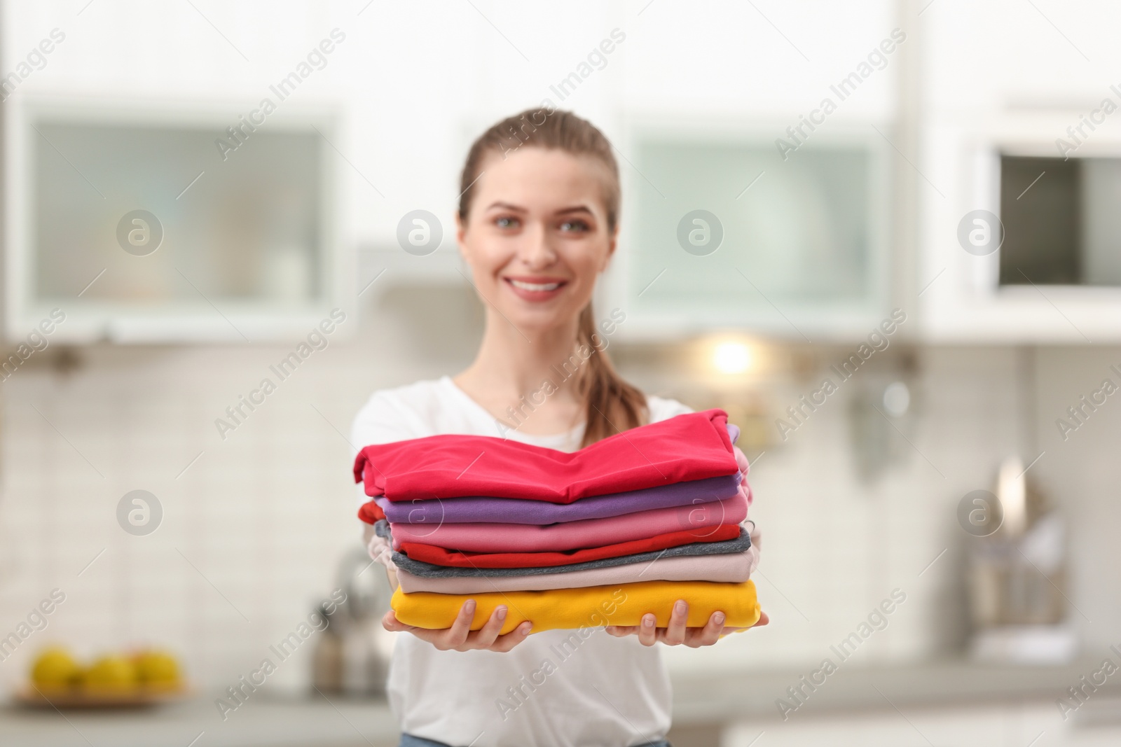 Photo of Woman holding folded clean clothes in kitchen. Laundry day