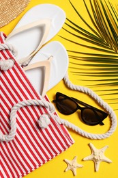 Flat lay composition with bag, palm leaf and other beach accessories on yellow background