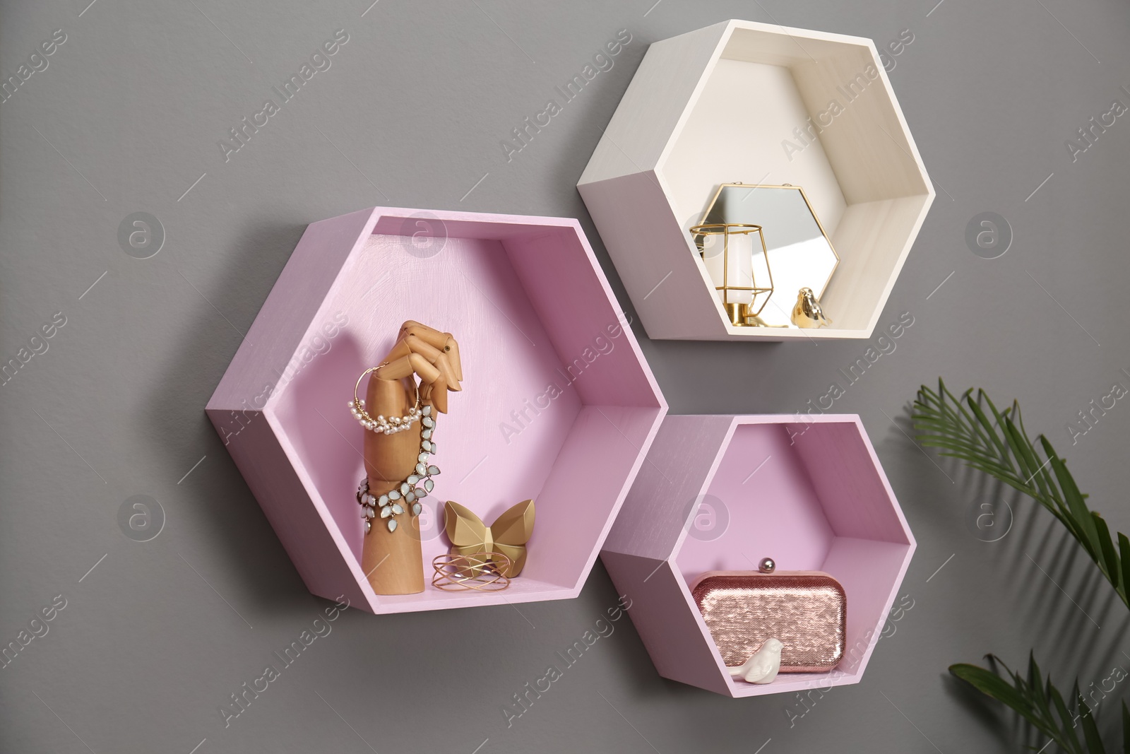 Photo of Hexagon shaped shelves with different stuff on grey wall. Interior design