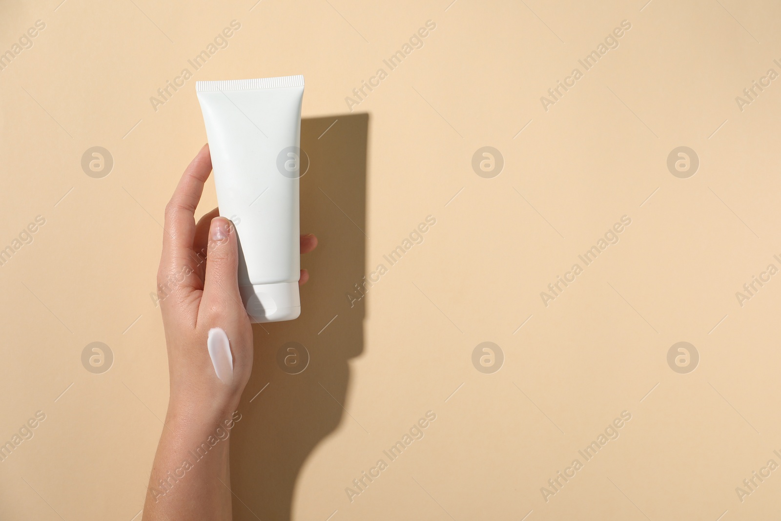 Photo of Woman with tube of hand cream on beige background, top view. Space for text