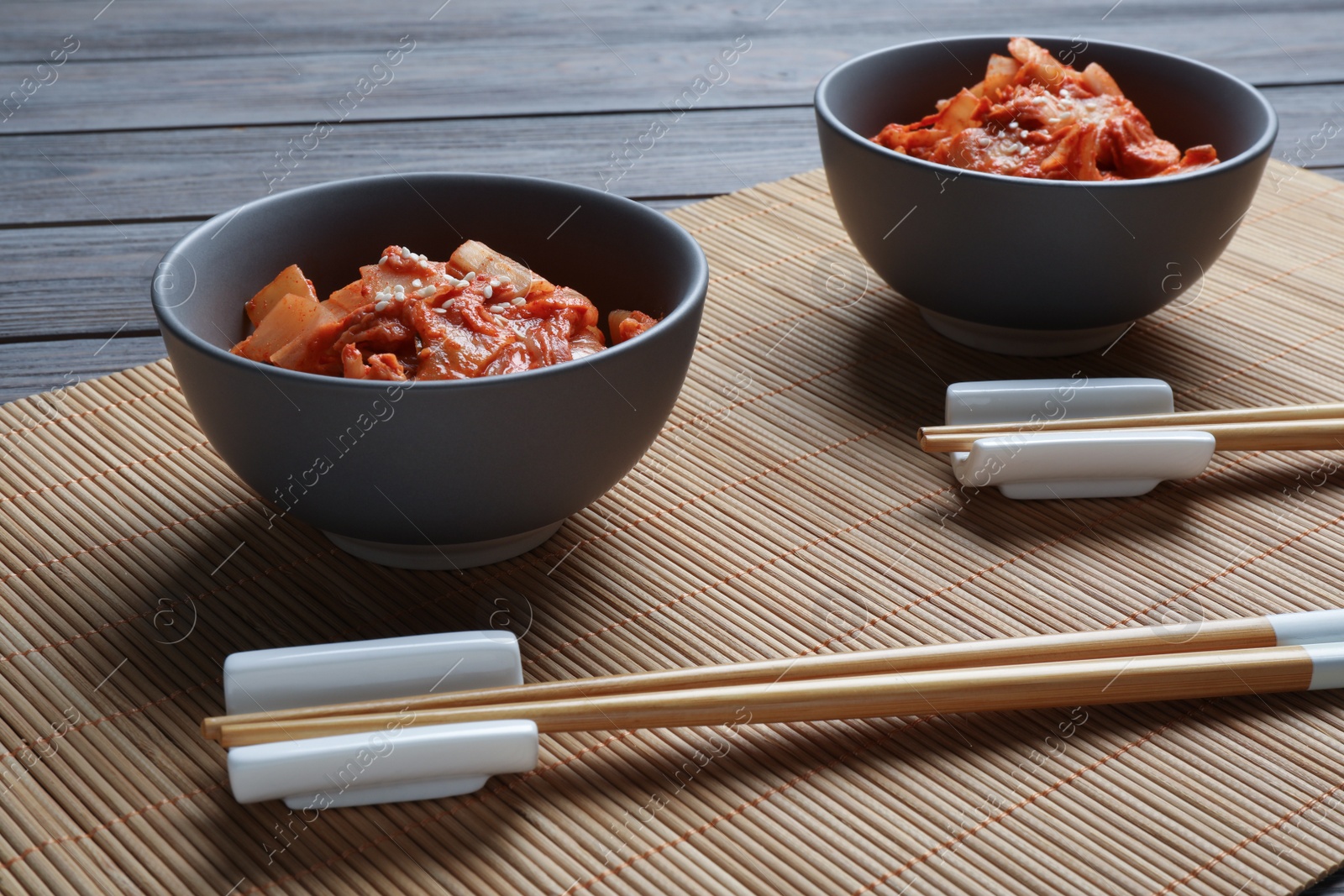 Photo of Bowls of spicy cabbage kimchi and chopsticks on bamboo mat