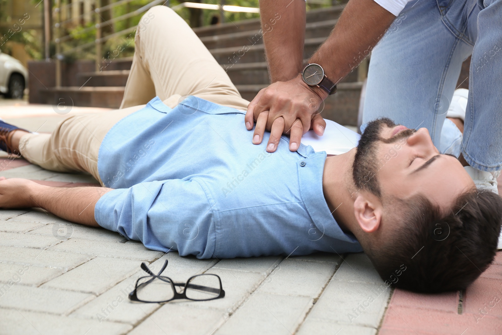 Photo of Passerby performing CPR on unconscious young man outdoors. First aid