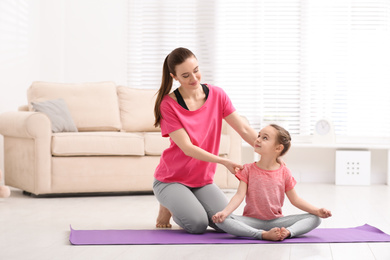 Photo of Young mother with little daughter practicing yoga at home