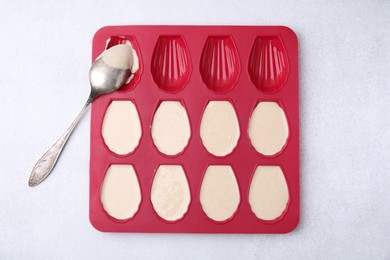 Photo of Baking mold for madeleine cookies with batter and spoon on white table, top view