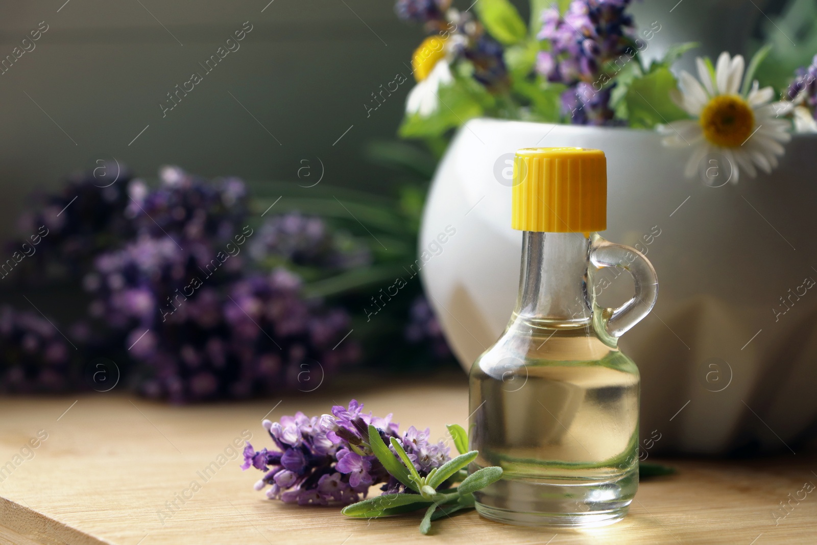 Photo of Bottle of natural lavender essential oil near mortar with flowers on wooden table, closeup. Space for text