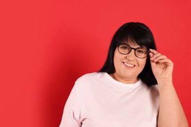 Beautiful overweight mature woman in eyeglasses on red background. Space for text