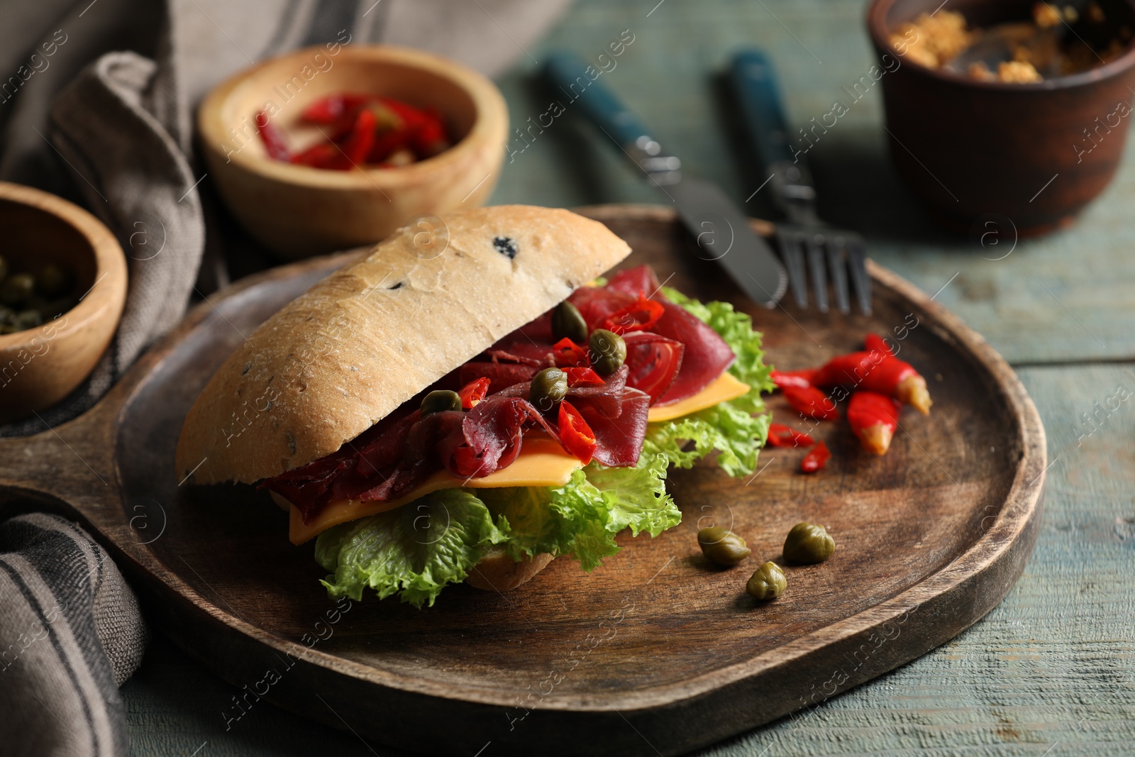 Photo of Delicious sandwich with bresaola, cheese and lettuce served on light blue wooden table, closeup