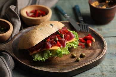 Photo of Delicious sandwich with bresaola, cheese and lettuce served on light blue wooden table, closeup