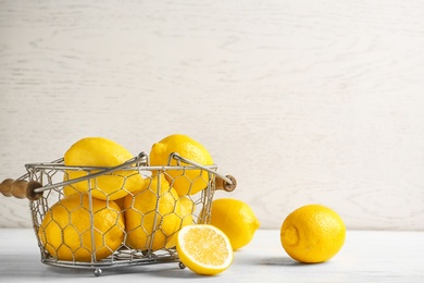 Photo of Basket with ripe lemons on table against light background