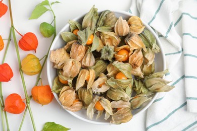 Photo of Ripe physalis fruits with dry husk and colorful sepals on white table, flat lay