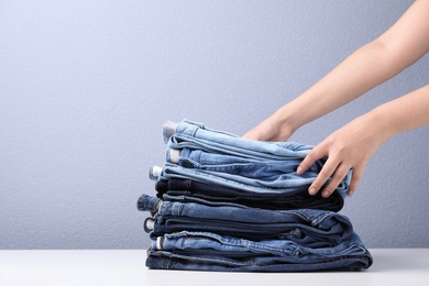 Young woman folding stylish jeans on table