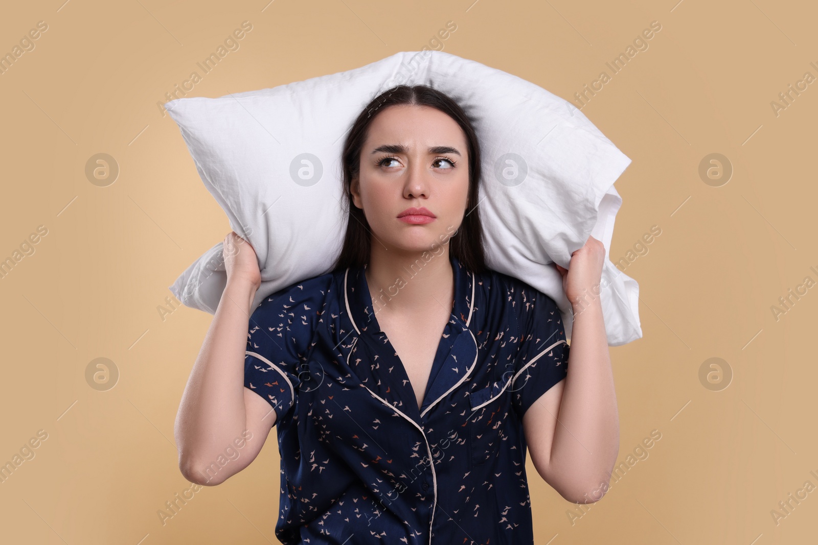 Photo of Tired young woman with pillow on beige background. Insomnia problem