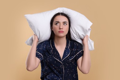 Tired young woman with pillow on beige background. Insomnia problem