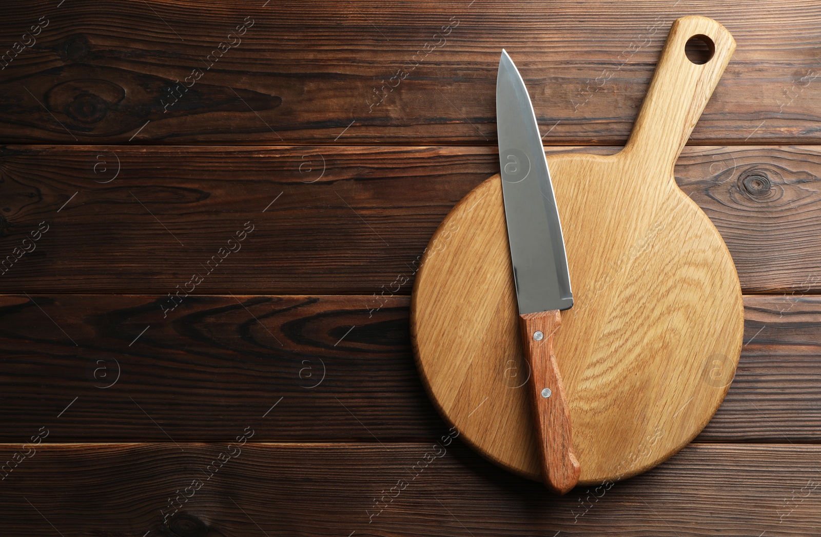 Photo of Knife and board on wooden table, top view. Space for text