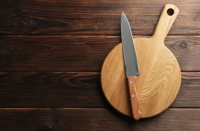 Photo of Knife and board on wooden table, top view. Space for text