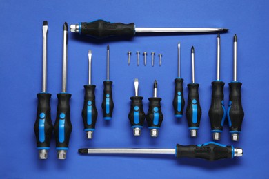 Photo of Set of screwdrivers and screws on blue background, flat lay