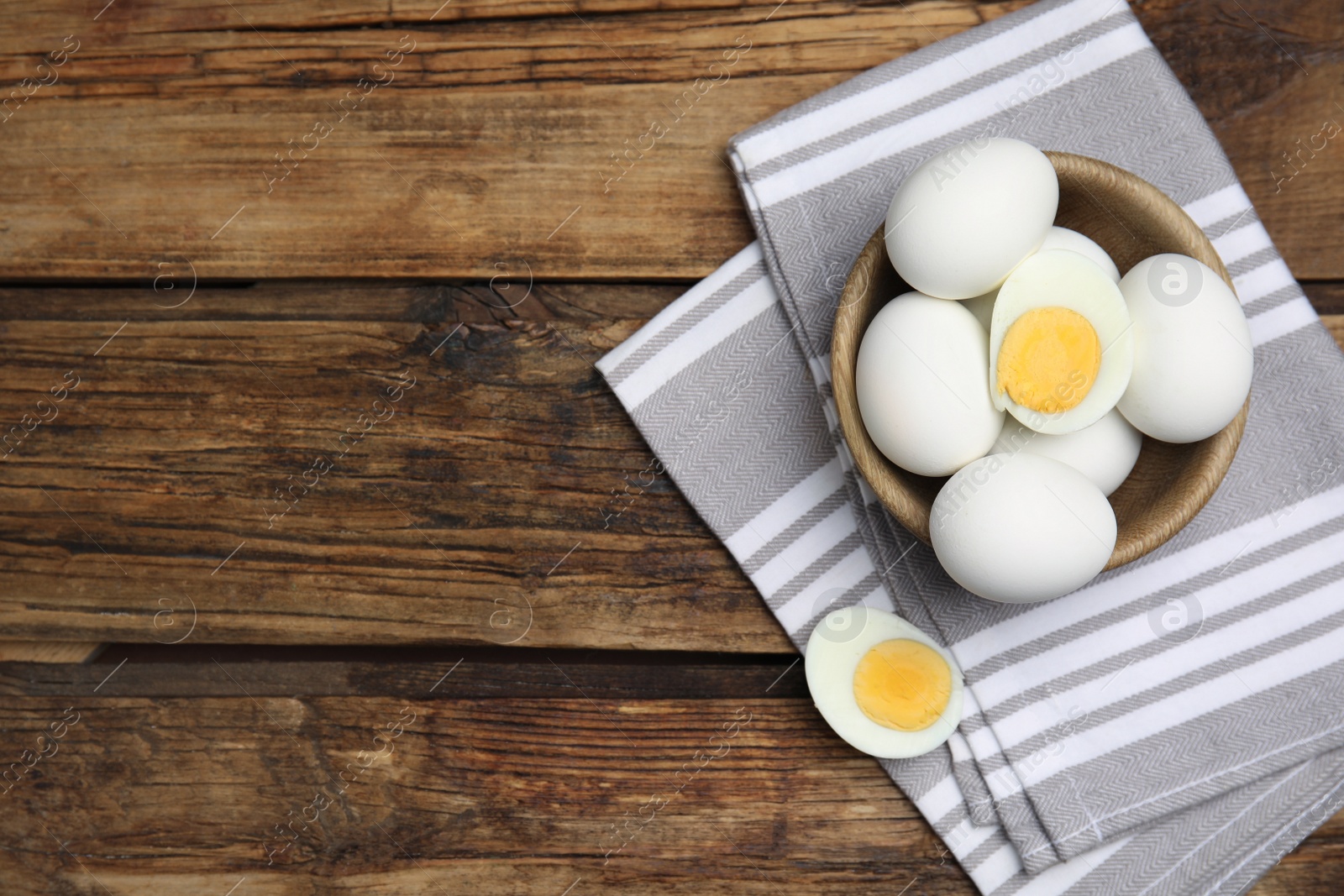 Photo of Bowl with hard boiled eggs and kitchen towel on wooden table, top view. Space for text