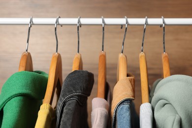 Hangers with stylish women`s clothes on rack near wooden wall, closeup